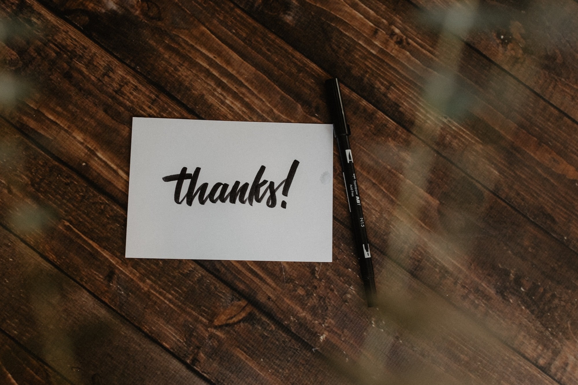 White card with thanks written on it sitting on a woodgrain desk with a pen next to it